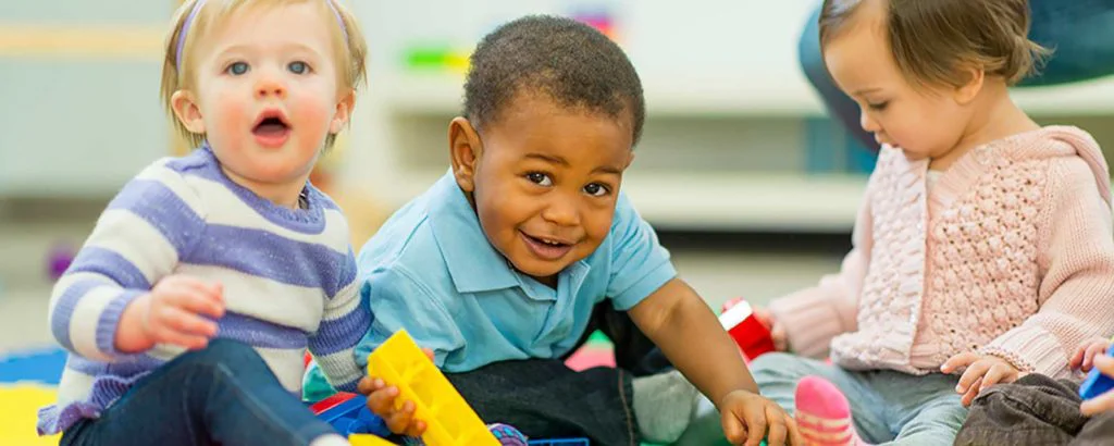 Three toddlers play with large blocks in quality child care environment