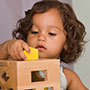 Toddler girl fitting shapes through matching slots on wooden box